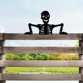 Black skeleton silhouette peeking over a wooden fence rail