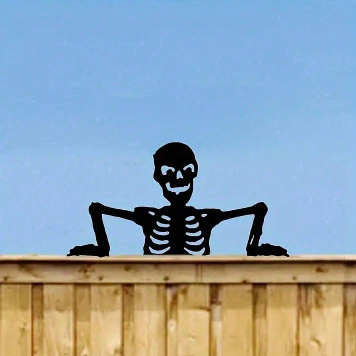 Black skeleton silhouette peeking over a fence against a blue sky