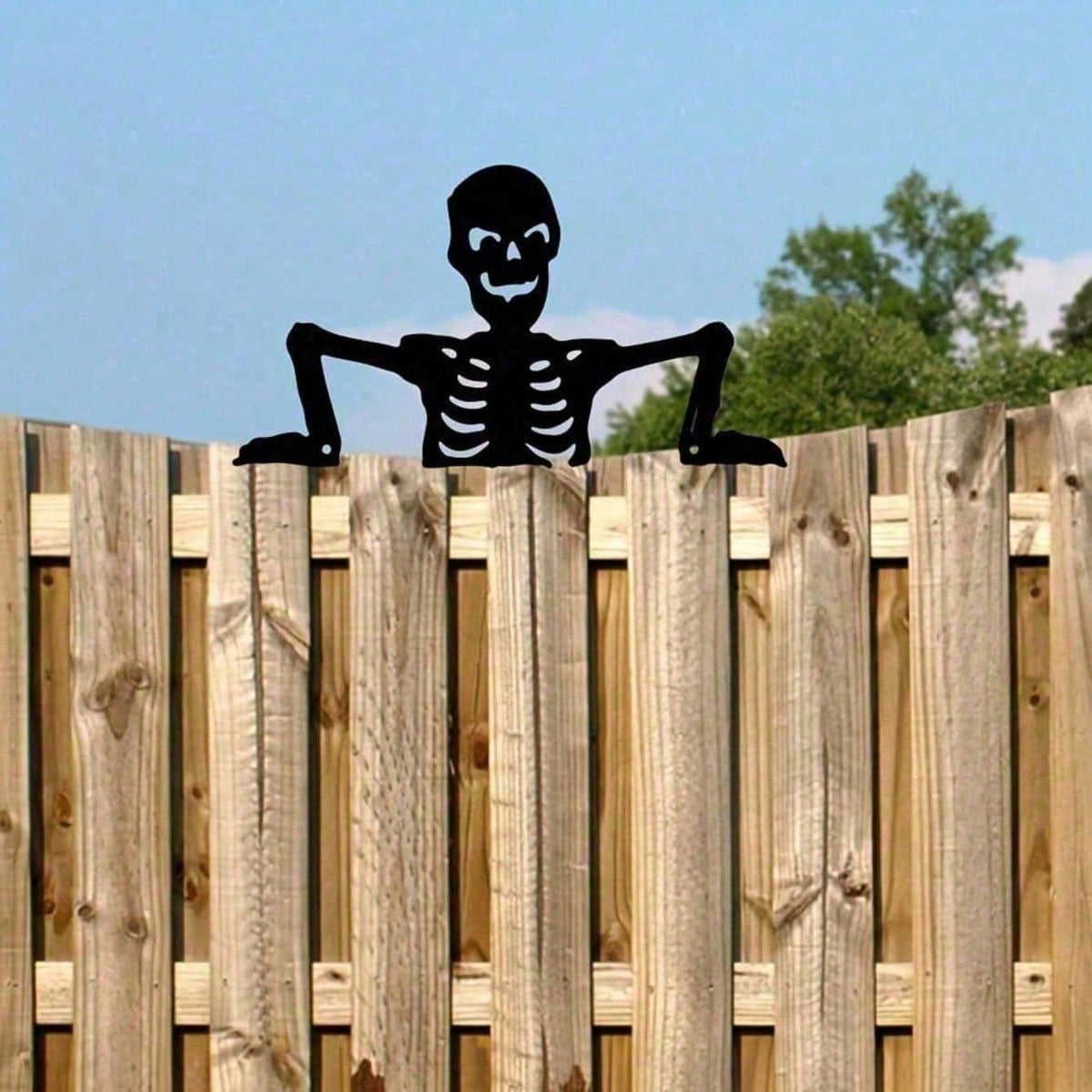 Black skeleton peeker on top of a wooden privacy fence