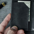Slim black wallet opened to the inner flap, with a folded bill tucked behind it